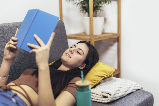 一个十几岁的女孩躺在沙发上看书。现代青少年在家。青少年文学概念。图片下载