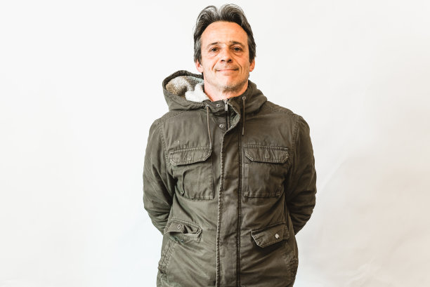 快乐的笑着的男人，微笑着的中年老人穿着绿色的夹克双臂交叉站在白色的墙上，肖像图片下载