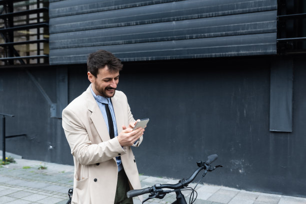 英俊时髦的商人一边打电话一边在城市里骑自行车。商务人士在办公楼前骑着自行车用智能手机安排午餐休息时间的会议或约会图片下载
