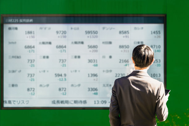 在股票板的电子公告栏上查看股票，用智能手机下达交易指令，管理资产的商人的背影图片下载