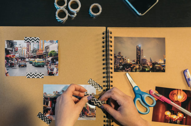 上图是一位无法辨认的中年妇女的手，她拿起一段washi胶带，准备制作手工制作的牛皮纸旅行相册。图片下载