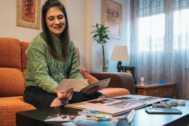 一位黑发的中年妇女微笑着看着这些照片，她将用水洗胶带制作她手工制作的牛皮纸旅行相册。图片下载