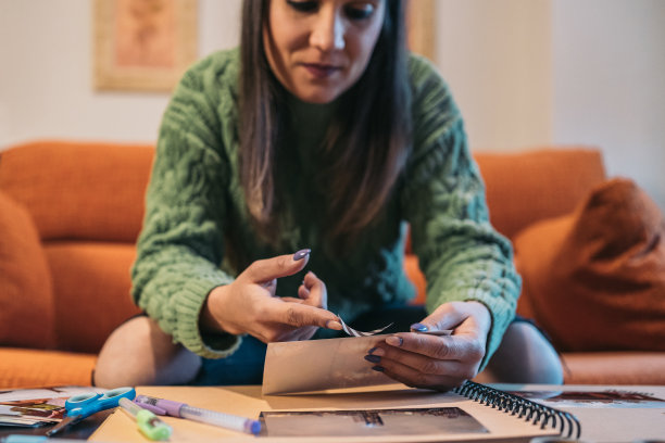 正面图片:一位中年妇女将一段washi胶带粘贴在她手工制作的牛皮纸旅行相册上。图片下载