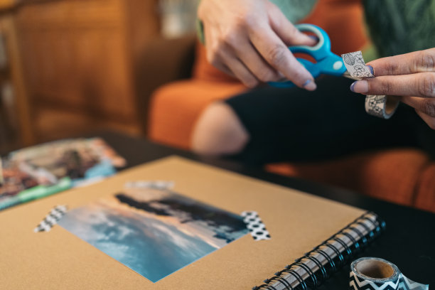 中年妇女的手剪出一小段washi胶带放在一张手工制作的旅行牛皮纸相册的封面照片上。图片下载