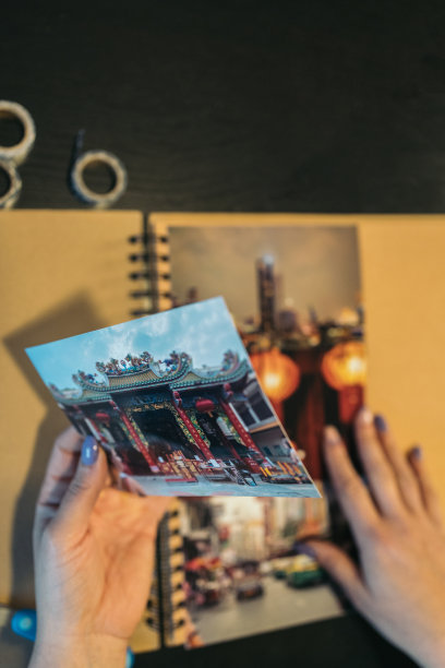 垂直图像，一个无法辨认的中年妇女的手放置照片，用washi胶带制作她手工制作的牛皮纸旅行相册。图片下载