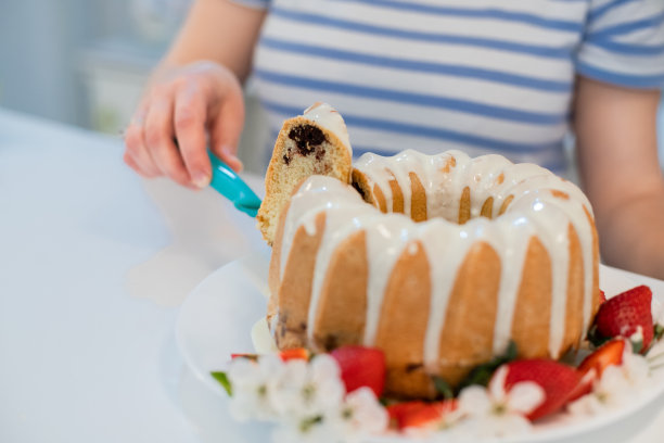 年轻女子正在切割装饰精美的春天主题的kugelhopf蛋糕，上面有花和草莓，并把它举起来展示图片下载