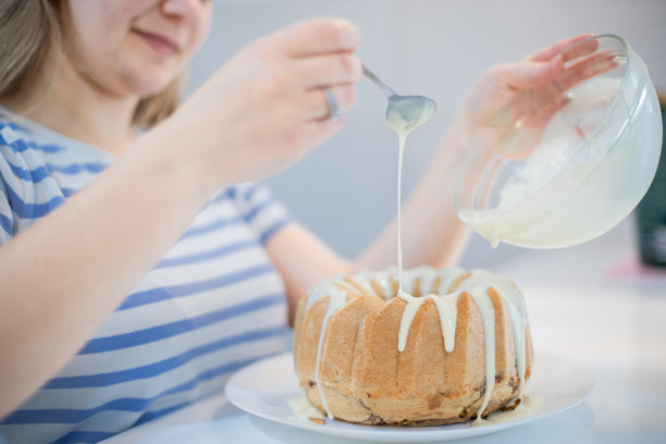 年轻女子正在装饰库格霍夫蛋糕，并把融化的白巧克力倒在上面图片下载