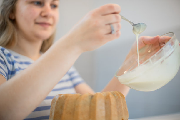 年轻女子正在装饰库格霍夫蛋糕，并把融化的白巧克力倒在上面图片下载
