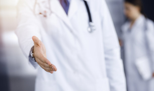在现代诊所里，不知名的男医生笔直地站着，伸出援助之手。女同事急着看医生的背景。医学的概念图片下载