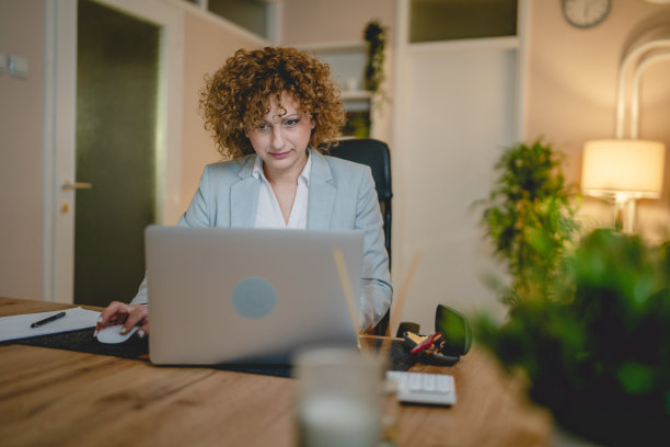 一个成熟的女人在家或办公室工作，坐在桌子旁使用笔记本电脑图片下载