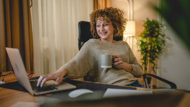 一个快乐的女人在家或办公室工作，坐在桌子旁使用笔记本电脑图片下载