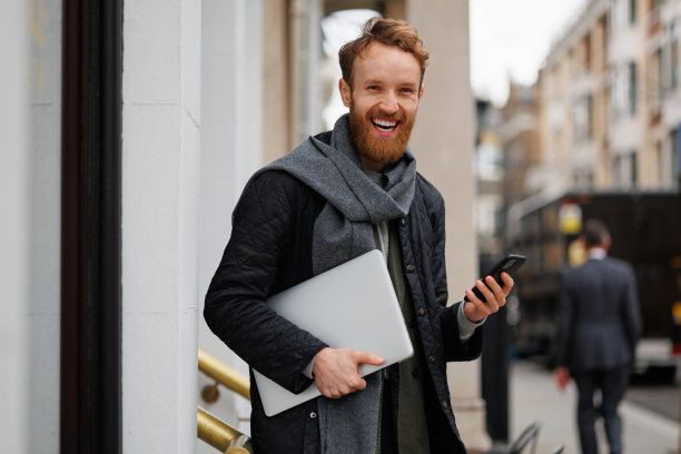 一个手里拿着笔记本电脑和智能手机的快乐商人站在大城市的街道上图片下载