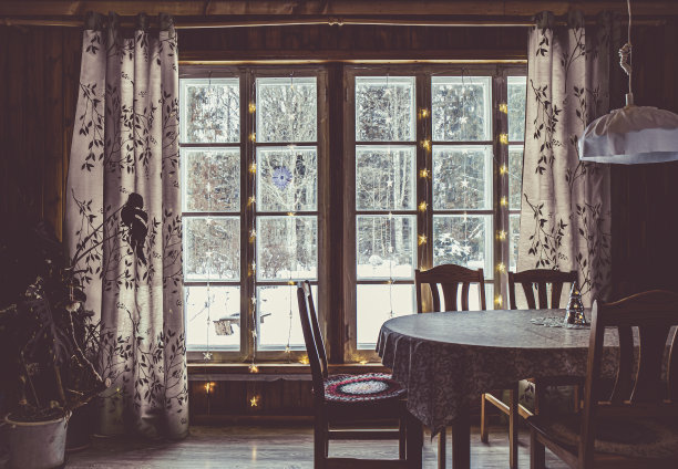 平房木质格子窗。黑暗，光线从窗户照射进来，背景是白雪覆盖的树木。室内的木桌和椅子。图片下载