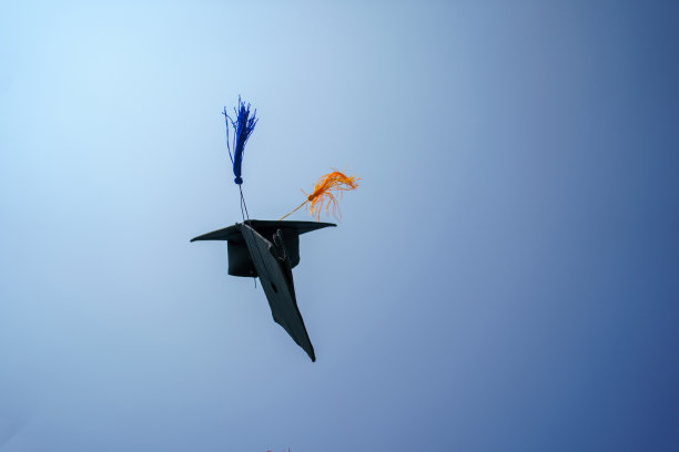 毕业典礼的特写大学高中毕业生在蓝天上扔帽子。图片下载