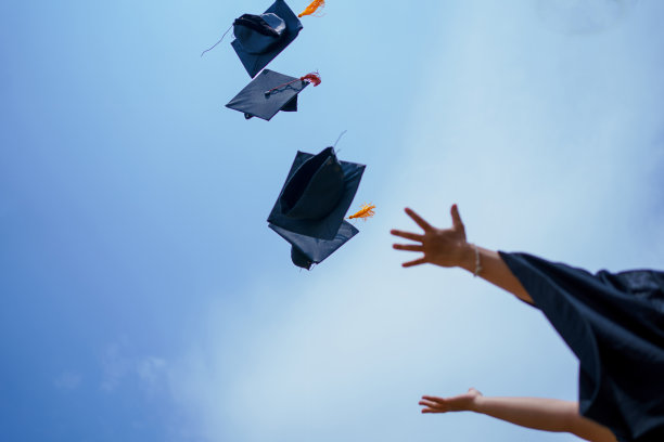毕业典礼的特写大学高中毕业生在蓝天上扔帽子。图片下载