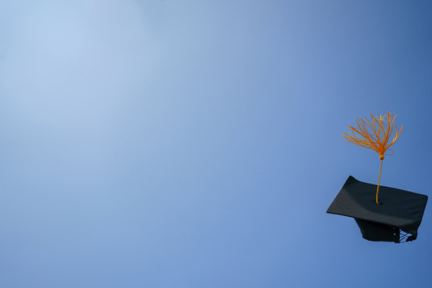 毕业典礼的特写大学高中毕业生在蓝天上扔帽子。图片下载