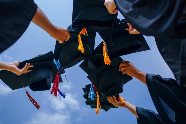 毕业典礼的特写大学高中毕业生在蓝天上扔帽子。图片下载