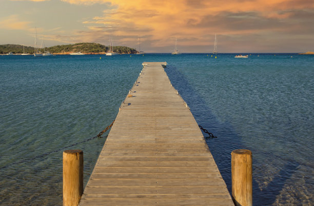 日落时分，朗迪纳拉海滩上绿松石蓝色的大海上的棕色木制码头图片下载