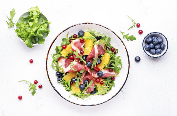 美味沙拉配烟熏鸭片，水果和浆果，芝麻菜和生菜，白色桌面背景，俯视图图片下载