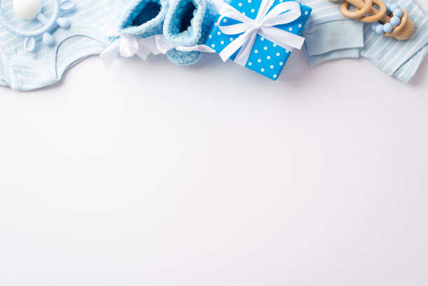 婴儿派对的概念。蓝色婴儿衣服的顶视图照片衬衫裤子针织靴礼盒与丝带蝴蝶结木制摇铃和牙齿在孤立的白色背景与copyspace图片下载