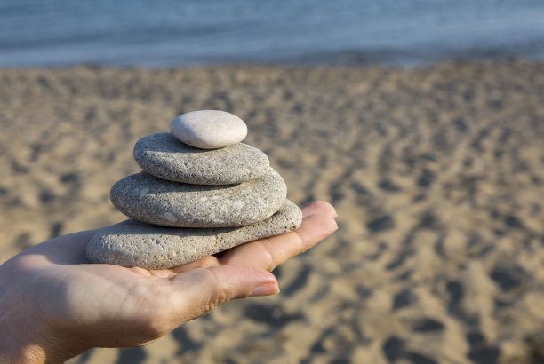在沙滩的背景下，女人手中堆积的鹅卵石呈金字塔状上升。图片下载
