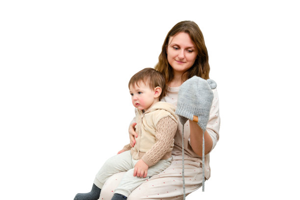 母亲给蹒跚学步的婴儿围上一条温暖的围巾，孤立在白色的背景上。一位母亲给孩子穿上保暖的衣服，在寒冷的天气里走冬天。一岁零三个月的孩子图片下载