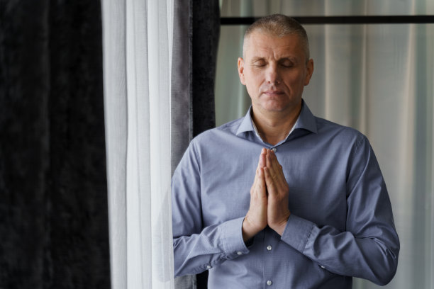 一个男人站在窗边做放松的呼吸练习。图片下载