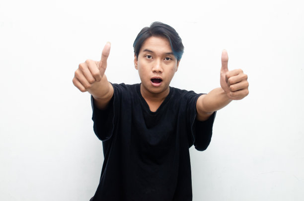 英俊迷人的亚洲男人，蓝色的头发，开心地微笑着，竖起大拇指，作为赞美，在白色的背景上孤立起来。男人通过竖起大拇指表示赞同和赞美。图片下载