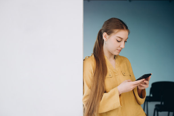 自信的女性商务人士手持智能手机站在工作场所的走廊上图片下载