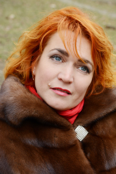 红头发的女人戴着白色的针织帽，穿着暖和的连帽休闲派克夹克外套，女孩在停车场，人行横道和汽车在背景中，女孩温暖冰冻的手图片下载