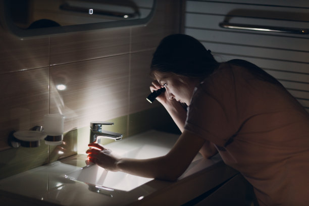 年轻女子在黑暗中手持手电筒在厨房的水槽和水龙头图片下载