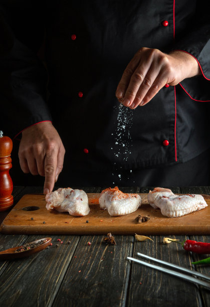 厨师在生鸡翅上加盐。在饭店或旅馆的厨房里煮鸡块的图片下载