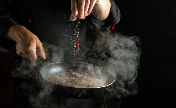 厨师在热煎锅中加入盐和香肠。黑色背景的酒店菜单或食谱概念图片下载