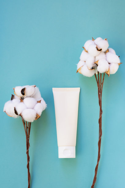 有机化妆品的概念，用棉花提取物作为超级寓言产品。蓝色背景上的单奶油色管与柔软的羊毛花棉细枝。图片下载