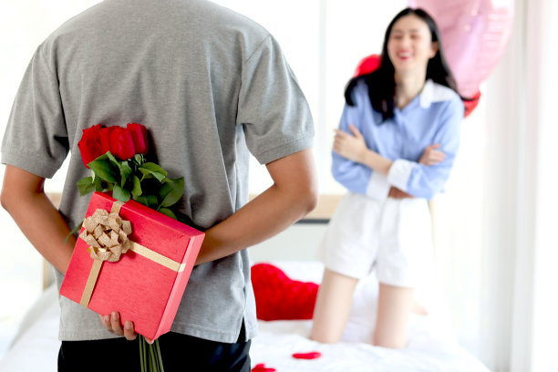 男人藏着红色的礼盒，背后放着美丽的红玫瑰花束，准备送给情人女友情人节礼物庆祝，情侣们制造惊喜，爱情和幸福。情人节快乐图片下载