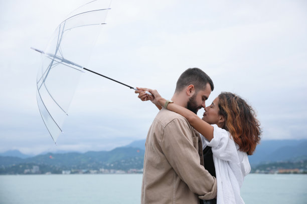 年轻夫妇撑着伞，在雨中享受在沙滩上聊天的时光图片下载