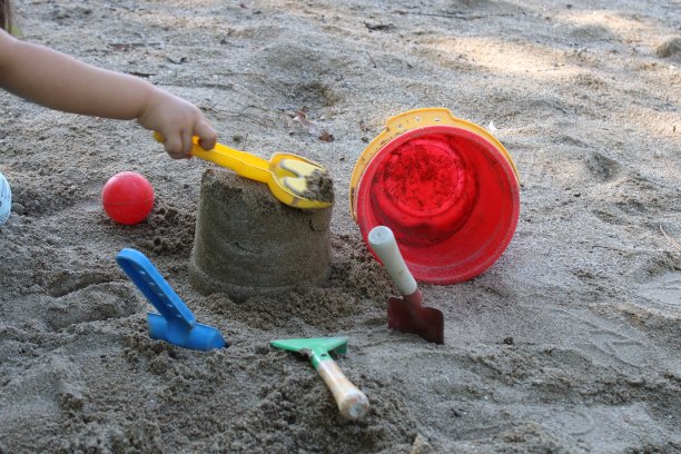 一个孩子拿着一把黄铲子在沙滩上玩耍。夏天的时间。海滩上孩子们的玩具图片下载