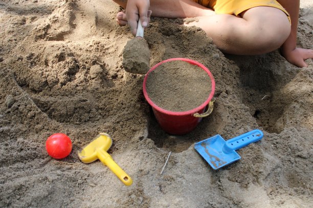 一个孩子拿着一把黄铲子在沙滩上玩耍。夏天的时间。海滩上孩子们的玩具图片下载