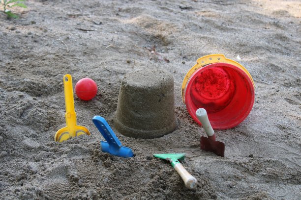 沙子里有一个水桶，旁边是一个红色的球和一个红色的玩具。夏天的时间。海滩上孩子们的玩具图片下载