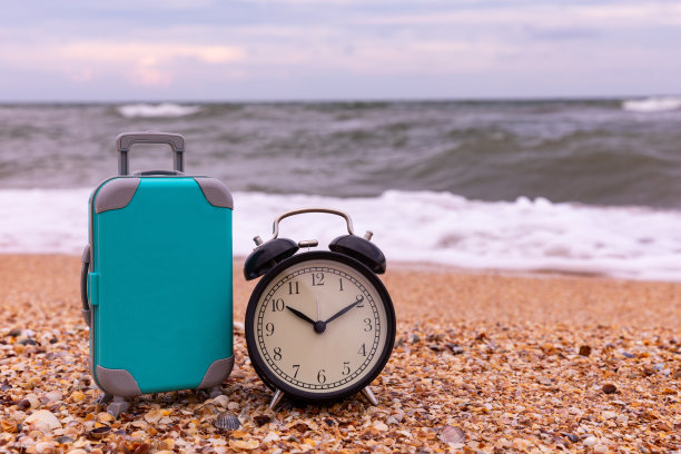 暑假概念。是时候放松了。闹钟带着行李箱在沙滩上。副本的空间。图片下载