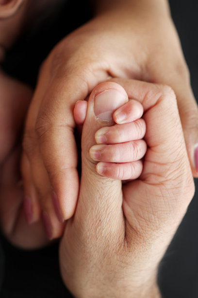 孩子的小手和父母的手的特写。新生儿出生后紧紧地抓着父母的手指。黑色背景的专业微距照片图片下载