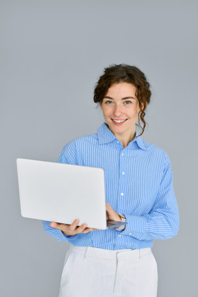年轻微笑的商务女经理使用笔记本电脑孤立在灰色，垂直。图片下载