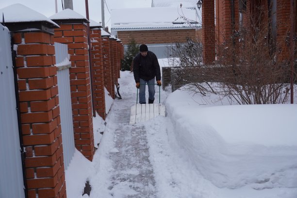 冬天，一名男子在房子的院子里清扫积雪图片下载