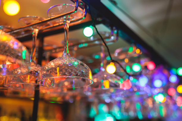 酒吧内部的细节，葡萄酒和不同的酒精鸡尾酒酒杯悬挂在吧台上，背景是酒瓶和调酒师，夜生活俱乐部有背光照明图片下载