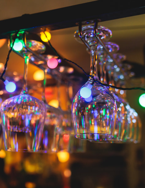 酒吧内部的细节，葡萄酒和不同的酒精鸡尾酒酒杯悬挂在吧台上，背景是酒瓶和调酒师，夜生活俱乐部有背光照明图片下载