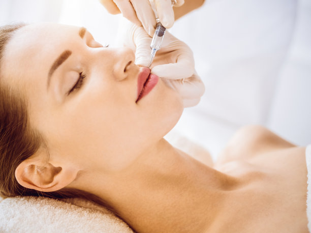在阳光明媚的医疗中心，美女闭着眼睛接受美容注射。美容师医生用注射器给女性面部做美容手术。美容医学和外科的概念图片下载