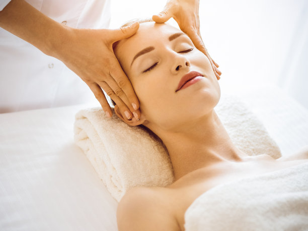 美丽的女人享受面部按摩与闭上眼睛在阳光水疗中心图片下载
