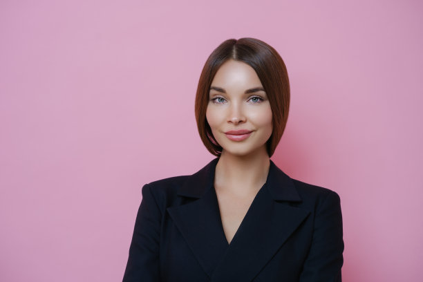 严肃愉快的黑发欧洲女人穿着黑色衣服，自信而满足地站着，淡妆，吸引人的样子，孤立在粉红色的工作室背景上。商务女士准备上班图片下载