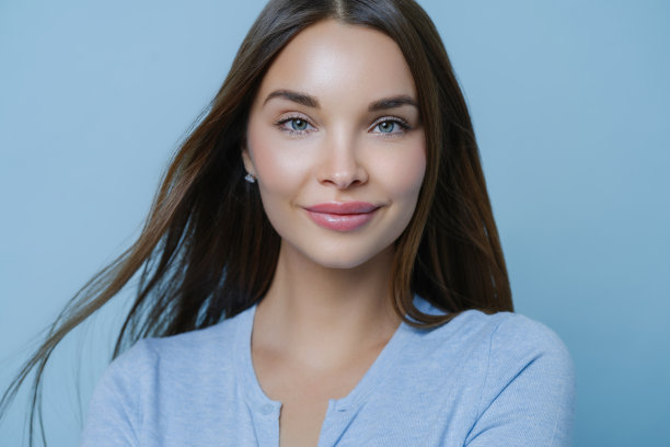 年轻女子的横拍，直发黑发，清新的面貌和妆容，关心自己的皮肤，满意的护肤品，在工作室室内留下积极的评论姿势。美,美容图片下载