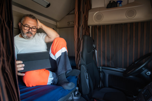 老卡车司机坐在卡车的床上，拉上窗帘，在他的空闲时间用平板电脑娱乐自己。图片下载